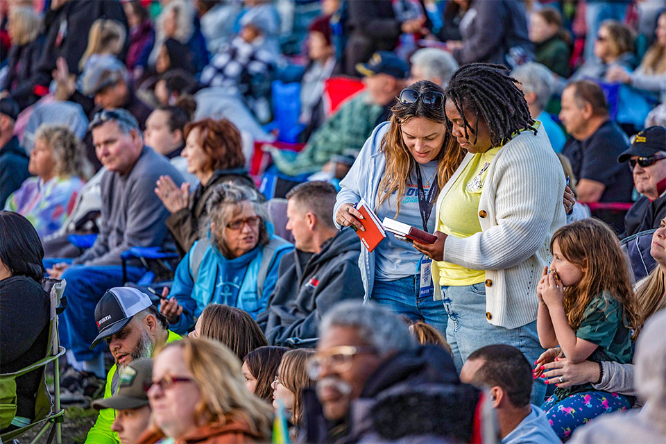 Prayer team volunteer handing out bible to woman.