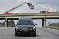 The hearse carrying the body of Billy Graham passes under an American flag as it drives toward the Billy Graham Library in Cherryville, N.C., Saturday, Feb. 24, 2018. Graham's body was brought to his hometown of Charlotte on Saturday, Feb. 24, as part of a procession expected to draw crowds of well-wishers. (AP Photo/Kathy Kmonicek, Pool)